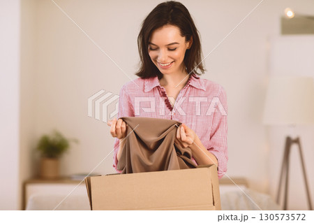 Moving Concept. Excited girl getting ready for moving out, packing clothes in paper box, copyspace Moving Concept. Excited girl getting ready for moving out, packing clothes in paper box, copyspace 130573572