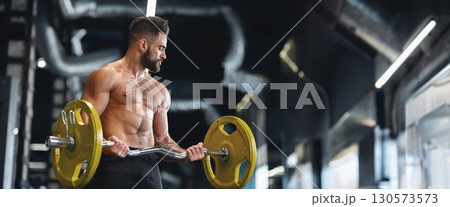Handsome naked weightlifter lifting heavy barbell in gym, free space, panorama 130573573