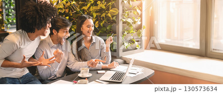 Happy young multiethnic entrepreneurs at cafe celebrating success or starting new project, looking at laptop together and shouting, empty space Happy young multiethnic entrepreneurs at cafe celebrating success or starting new project, looking at laptop together and shouting, empty space 130573634