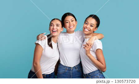 Girls Friendship. Three Happy Multiracial Women Hugging Smiling At Camera Standing Over Turquoise Background. Studio Shot Girls Friendship. Three Happy Multiracial Women Hugging Smiling At Camera Standing Over Turquoise Background. Studio Shot 130573720