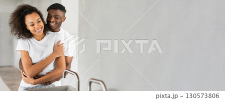 A joyful black couple shares a warm embrace while standing close in a bright, stylish indoor space. Their smiles highlight a moment of love and connection as they enjoy each other company. A joyful black couple shares a warm embrace while standing close in a bright, stylish indoor space. Their smiles highlight a moment of love and connection as they enjoy each other company. 130573806