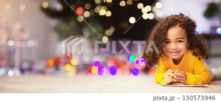 Christmas fun. Adorable little afro girl lying on floor near Xmas tree, empty space Christmas fun. Adorable little afro girl lying on floor near Xmas tree, empty space 130573946