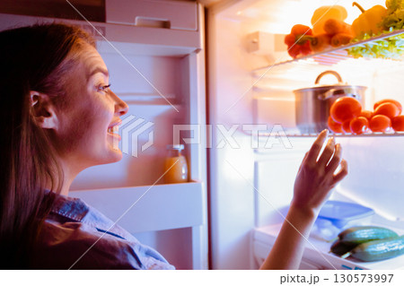 Healthy diet. Millennial housewife choosing vegetable for late dinner in fridge, free space Healthy diet. Millennial housewife choosing vegetable for late dinner in fridge, free space 130573997