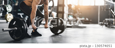 Hard strength workout. Muscular powerlifter lifting heavy barbell from gym floor, empty space, cropped 130574051