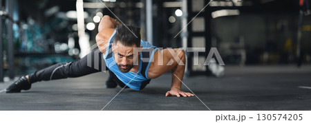 Strength exercise. Muscular man doing push ups on on hands in gym, panorama with copy space 130574205