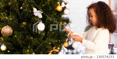 Christmas tradition. Little afro girl decorating Xmas tree at home, free space Christmas tradition. Little afro girl decorating Xmas tree at home, free space 130574233