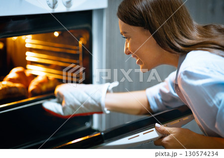 Tasty and simple lunch. Cheerful housewife taking roasted chicken out of oven at home Tasty and simple lunch. Cheerful housewife taking roasted chicken out of oven at home 130574234