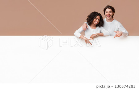Place for your ad. Joyful interracial couple leaning and pointing at white advertisement board with free space for your text Place for your ad. Joyful interracial couple leaning and pointing at white advertisement board with free space for your text 130574283