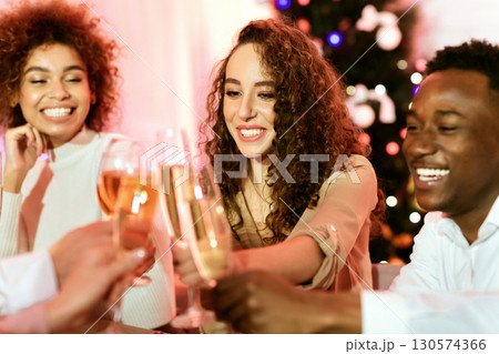 Celebrating New Year. Diverse Friends Toasting And Clinking Glasses Smiling Sitting At Celebratory Table Indoor. Selective Focus Celebrating New Year. Diverse Friends Toasting And Clinking Glasses Smiling Sitting At Celebratory Table Indoor. Selective Focus 130574366