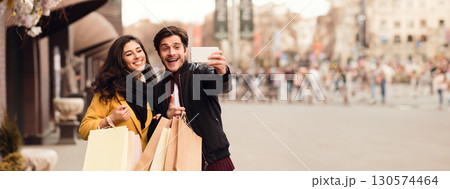 Couple recording video for fashion blog after shopping in mall, walking outdoors, panorama with copy space Couple recording video for fashion blog after shopping in mall, walking outdoors, panorama with copy space 130574464