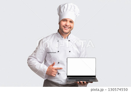 Chef Man Holding Laptop With Blank Screen Pointing Finger Standing Over White Studio Background. Cooking And Recipes Website. Panorama Chef Man Holding Laptop With Blank Screen Pointing Finger Standing Over White Studio Background. Cooking And Recipes Website. Panorama 130574550