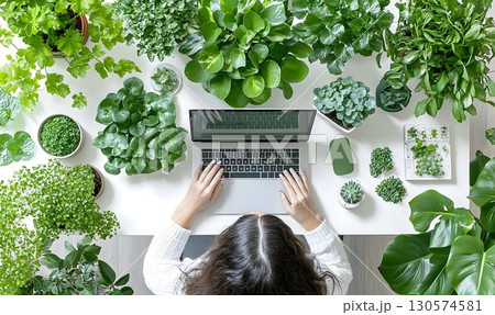 Woman Working on Laptop Surrounded by Lush Green Plants in Brigh 130574581