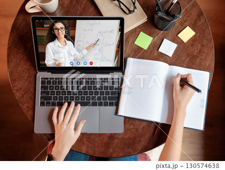 Distance Education Concept. Above top view of female student sitting at desk, writing in notebook, taking notes, using laptop, having online class with teacher. Remote studying from home, quarantine Distance Education Concept. Above top view of female student sitting at desk, writing in notebook, taking notes, using laptop, having online class with teacher. Remote studying from home, quarantine 130574638