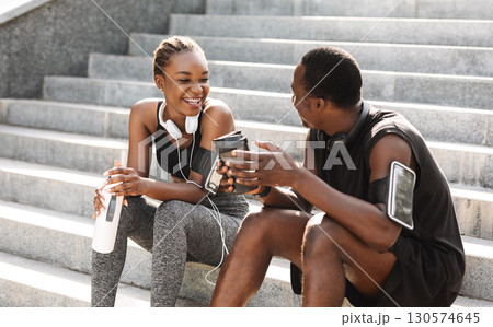 Fit Black Couple Taking Rest After Workout Outdoors, Sitting On Urban Stairs, Drinking Water And Coffee And Chatting, Free Space 130574645