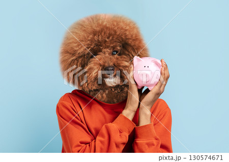 A playful moment captures an individual with a fluffy dog head, holding a pink piggy bank closely. The backdrop features a light blue hue, enhancing the whimsical atmosphere. A playful moment captures an individual with a fluffy dog head, holding a pink piggy bank closely. The backdrop features a light blue hue, enhancing the whimsical atmosphere. 130574671