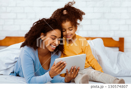 Family Weekend. Happy African American Mother And Daughter Using Tablet Computer Together Lying In Bed At Home. Family Weekend. Happy African American Mother And Daughter Using Tablet Computer Together Lying In Bed At Home. 130574807
