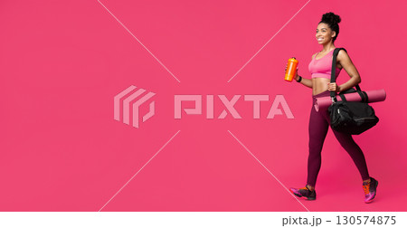 On a way to gym. Beautiful afro woman with yoga mat, sporty bag and shaker in hand going towards copy space 130574875