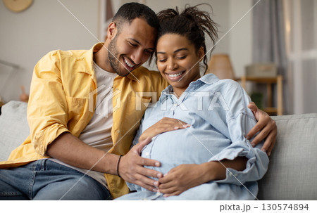 Pregnancy. Black Husband And Pregnant Wife Hugging Sitting At Home. Family Couple Expecting Baby, Man Embracing Woman Smiling Posing Together. Childbirth Concept 130574894