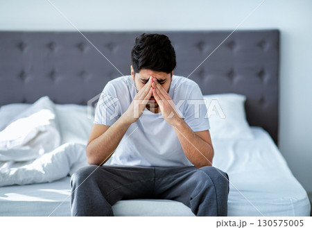 Male depression. Unhappy arab man sitting on bed and thinking about problems, closing face with hands, copy space. Stress, apathy and mental health issue concept. Male depression. Unhappy arab man sitting on bed and thinking about problems, closing face with hands, copy space. Stress, apathy and mental health issue concept. 130575005