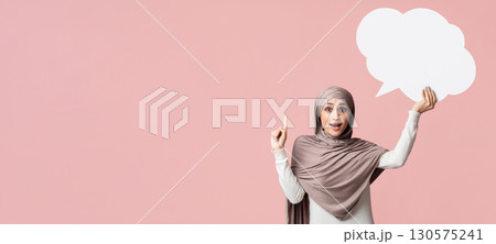 I have idea. Excited muslim girl holding empty speech bubble and pointing finger up over pink background, free space I have idea. Excited muslim girl holding empty speech bubble and pointing finger up over pink background, free space 130575241
