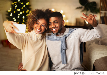 Happy black couple making selfie on Christmas eve, man showing peace gesture 130575264