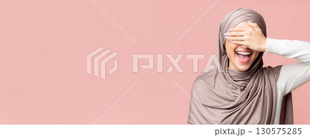Happy Muslim Girl In Hijab Covering Eyes With Hand And Smiling, Having Fun Over Pink Background, Free Space 130575285