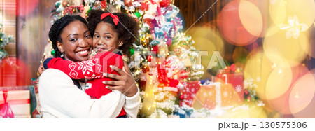 Portrait of happy black mother and little daughter posing near Christmas tree, cuddling and smiling at camera, panorama Portrait of happy black mother and little daughter posing near Christmas tree, cuddling and smiling at camera, panorama 130575306