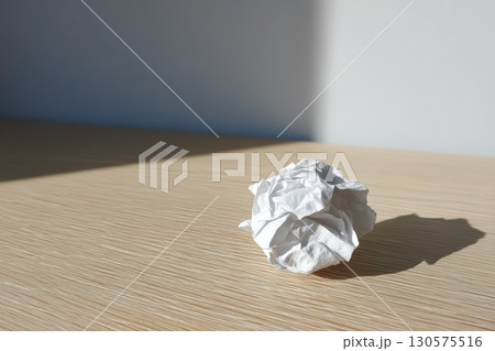 Crumpled white paper ball resting on a wooden surface in bright morning light 130575516