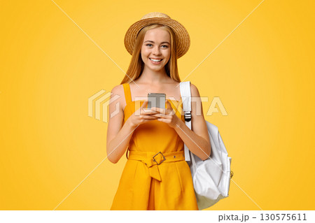 Online Map App Concept. Young Girl Tourist Holding Smartphone In Hands, Wearing Hat And Backpack, Posing Over Yellow Studio Background Online Map App Concept. Young Girl Tourist Holding Smartphone In Hands, Wearing Hat And Backpack, Posing Over Yellow Studio Background 130575611