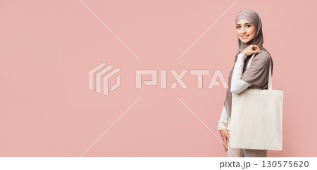 Eco Bag. Smiling Muslim Girl In Hijab With Blank Canvas Tote Handbag Over Pink Studio Background, Free Space Eco Bag. Smiling Muslim Girl In Hijab With Blank Canvas Tote Handbag Over Pink Studio Background, Free Space 130575620