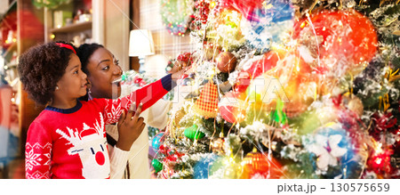 Little african american girl helping mother to decorate family Christmas tree, enjoying winter holidays together. Little african american girl helping mother to decorate family Christmas tree, enjoying winter holidays together. 130575659