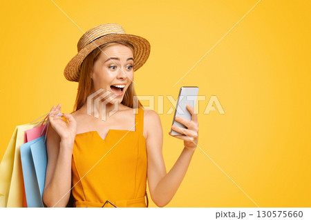 Discount App. Joyful Teen Girl In Straw Hat Looking At Smartphone Screen With Amazement 130575660