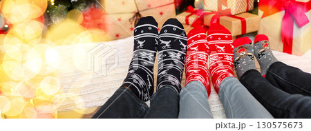 Christmas atmosphere background. Three pairs of feet in warm socks with winter holiday print ornament, panorama 130575673