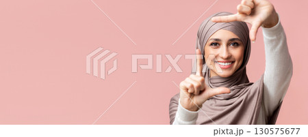 Frame your beauty. Smiling muslim girl in hijab making frame with fingers, capturing moment, posing over pink background with empty space Frame your beauty. Smiling muslim girl in hijab making frame with fingers, capturing moment, posing over pink background with empty space 130575677