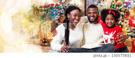 Christmas Family. Portrait of happy african dad, mom and daughter near the Xmas tree at home and smiling at camera. Christmas Family. Portrait of happy african dad, mom and daughter near the Xmas tree at home and smiling at camera. 130575681
