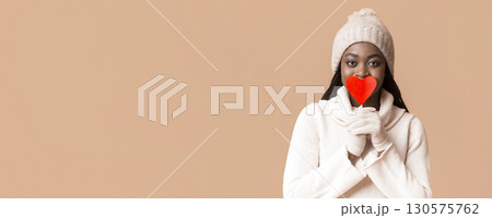 Be my valentine. Mysterious african winter woman covering her lips with valentine card over beige background, panorama with copy space Be my valentine. Mysterious african winter woman covering her lips with valentine card over beige background, panorama with copy space 130575762