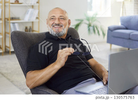 Happy senior man with laptop at home office chair, taking break with glasses Happy senior man with laptop at home office chair, taking break with glasses 130575763