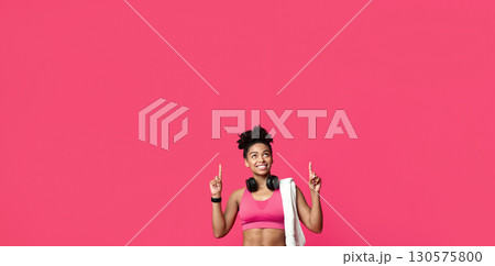 New ladies gym opening. Happy african american sporty girl with towel and earphones pointing up over red background 130575800