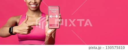 Cropped of smiling afro fitness lady pointing at workout application on mobile phone screen, red background, free space 130575810