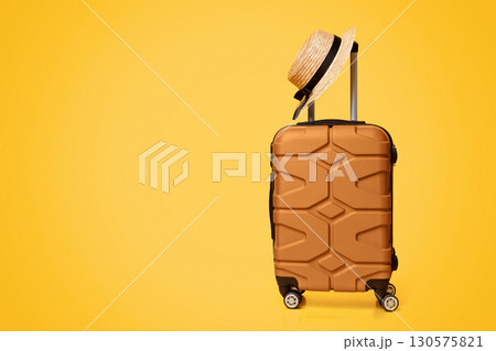 Travel Concept. Hand luggage suitcase with hat on it over yellow studio background with copy space 130575821