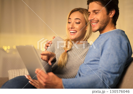 Happy couple searching gifts for christmas and using digital tablet, spending cold evening at home Happy couple searching gifts for christmas and using digital tablet, spending cold evening at home 130576046