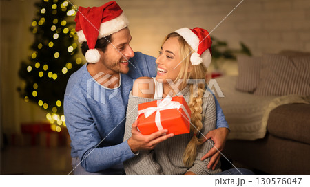 Christmas gift. Happy couple celebrating Christmas at home, man giving present to wife Christmas gift. Happy couple celebrating Christmas at home, man giving present to wife 130576047