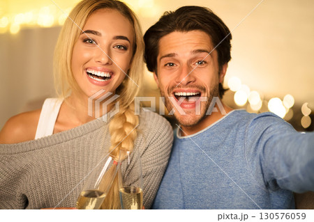 Beautiful couple making selfie and clinking champagne glasses at cozy winter evening at home Beautiful couple making selfie and clinking champagne glasses at cozy winter evening at home 130576059