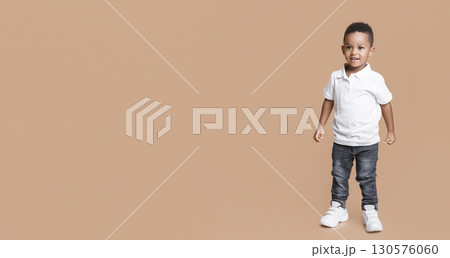 Full length portrait of smiling little black boy in jeans and white t-shirt on yellow studio background 130576060