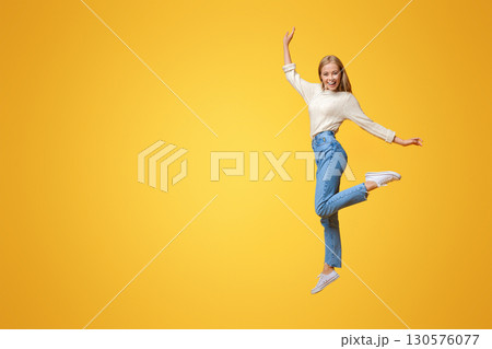 Carefree youth. Happy young girl jumping on air and smiling over orange background Carefree youth. Happy young girl jumping on air and smiling over orange background 130576077