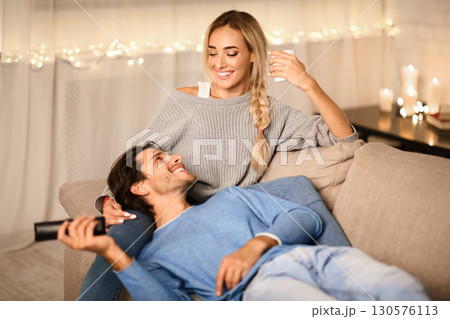 Young couple enjoying winter holidays, talking and watching tv on sofa in cozy room Young couple enjoying winter holidays, talking and watching tv on sofa in cozy room 130576113