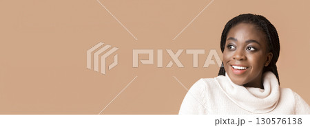 A young African American woman with braided hair smiles brightly, showcasing her joy and confidence. She is dressed in a cozy, light sweater, looking at copy space A young African American woman with braided hair smiles brightly, showcasing her joy and confidence. She is dressed in a cozy, light sweater, looking at copy space 130576138