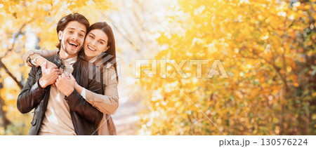 Positive woman hugging her happy man from behind, posing at autumn park, copy space 130576224