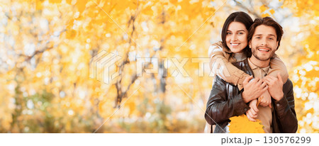 Happy girl in love hugging her cheerful man from behind, posing at autumn forest, copy space Happy girl in love hugging her cheerful man from behind, posing at autumn forest, copy space 130576299