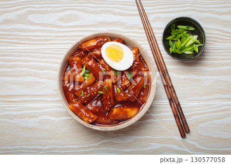 Traditional Korean tteokbokki served in white bowl with chopsticks and sesame seeds on white wooden rustic background 130577058